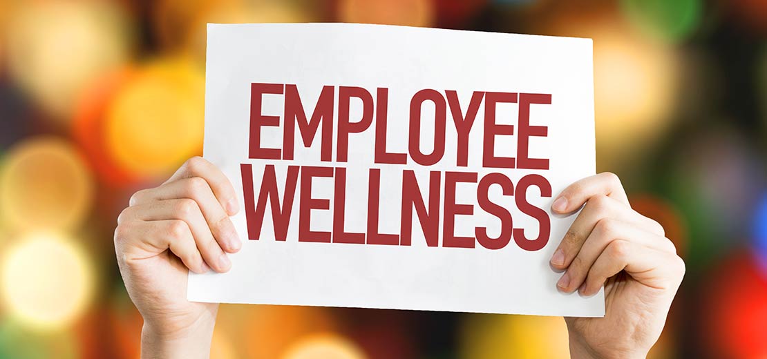 Employee holding an Employee Wellness sign. Promoting employee wellness programs in our Boise, Garden City, Meridian, Nampa, Idaho Falls, Pocatello and Rexburg locations.