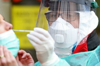 Masked and gowned lab worker taking a sample for COVID-19 testing.