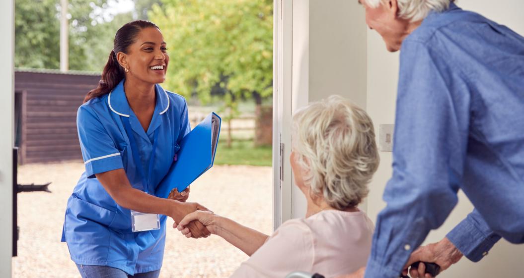 A medical laboratory technician being welcomed by a home-bound elderly couple.