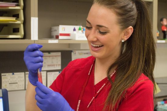 Phlebotomist with collected sample in laboratory. Smiling at successful draw.